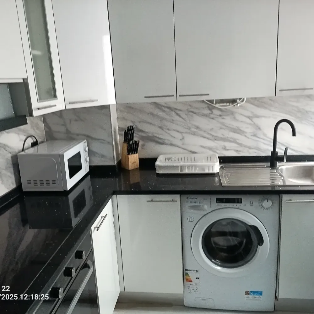 Cocina moderna con armarios blancos, encimera negra, microondas, fregadero y lavadora.