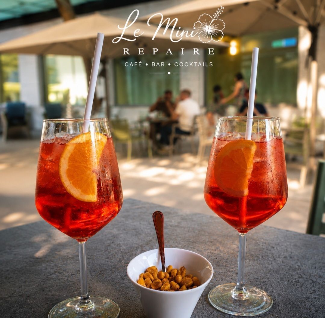 Deux cocktails rouges avec des tranches d'orange sur une table de café en terrasse, à côté d'un petit bol de snacks.