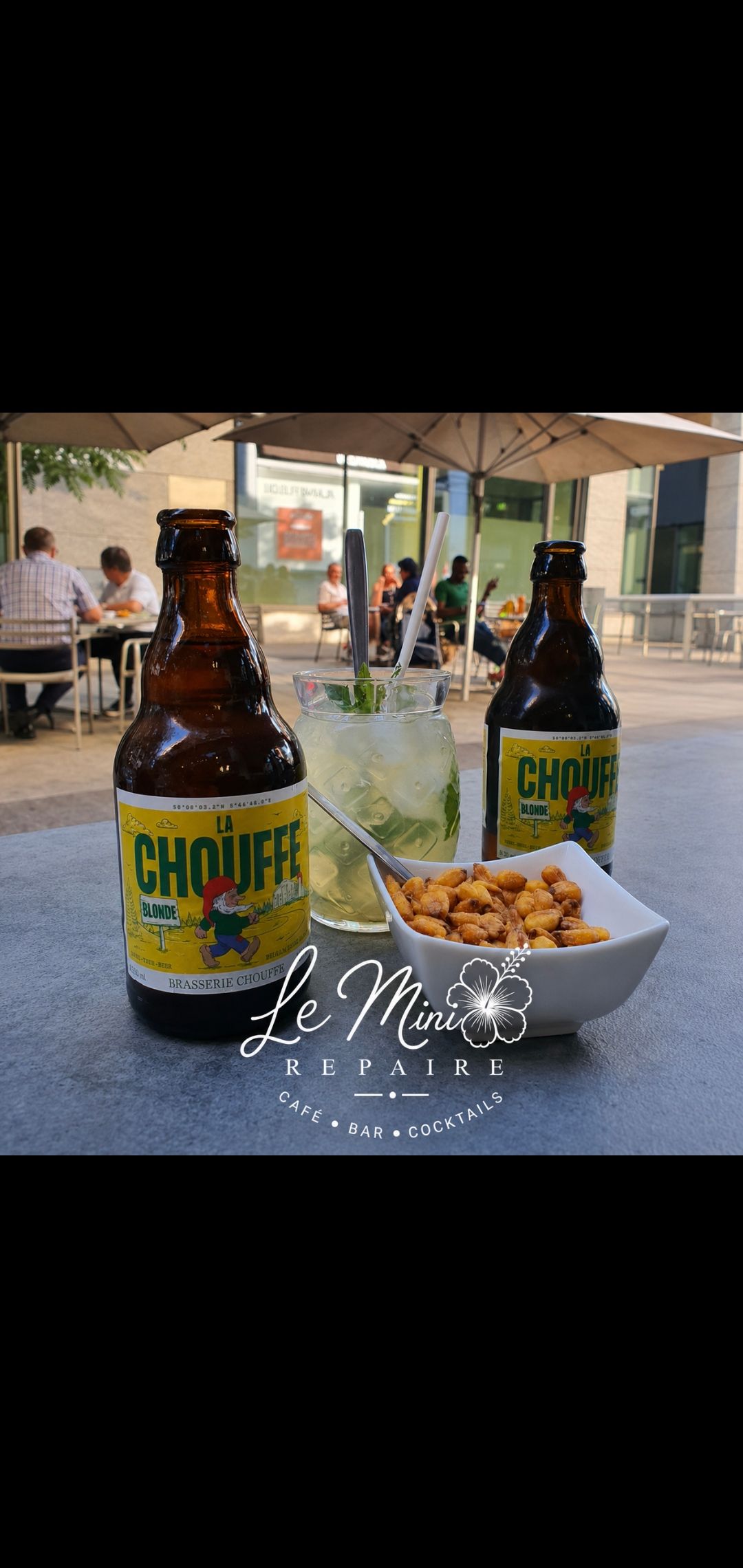 Deux bouteilles de bière et un bol de snacks sur une table à la terrasse d'un café.