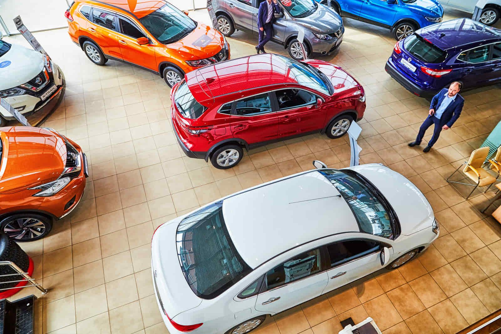 Autos de varios colores exhibidos en la sala de exposición de un concesionario de automóviles, mientras la gente los observa.