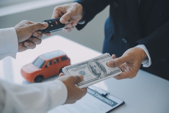 Manos intercambiando llaves de auto y dinero en efectivo sobre una mesa, con un modelo de auto de juguete visible.
