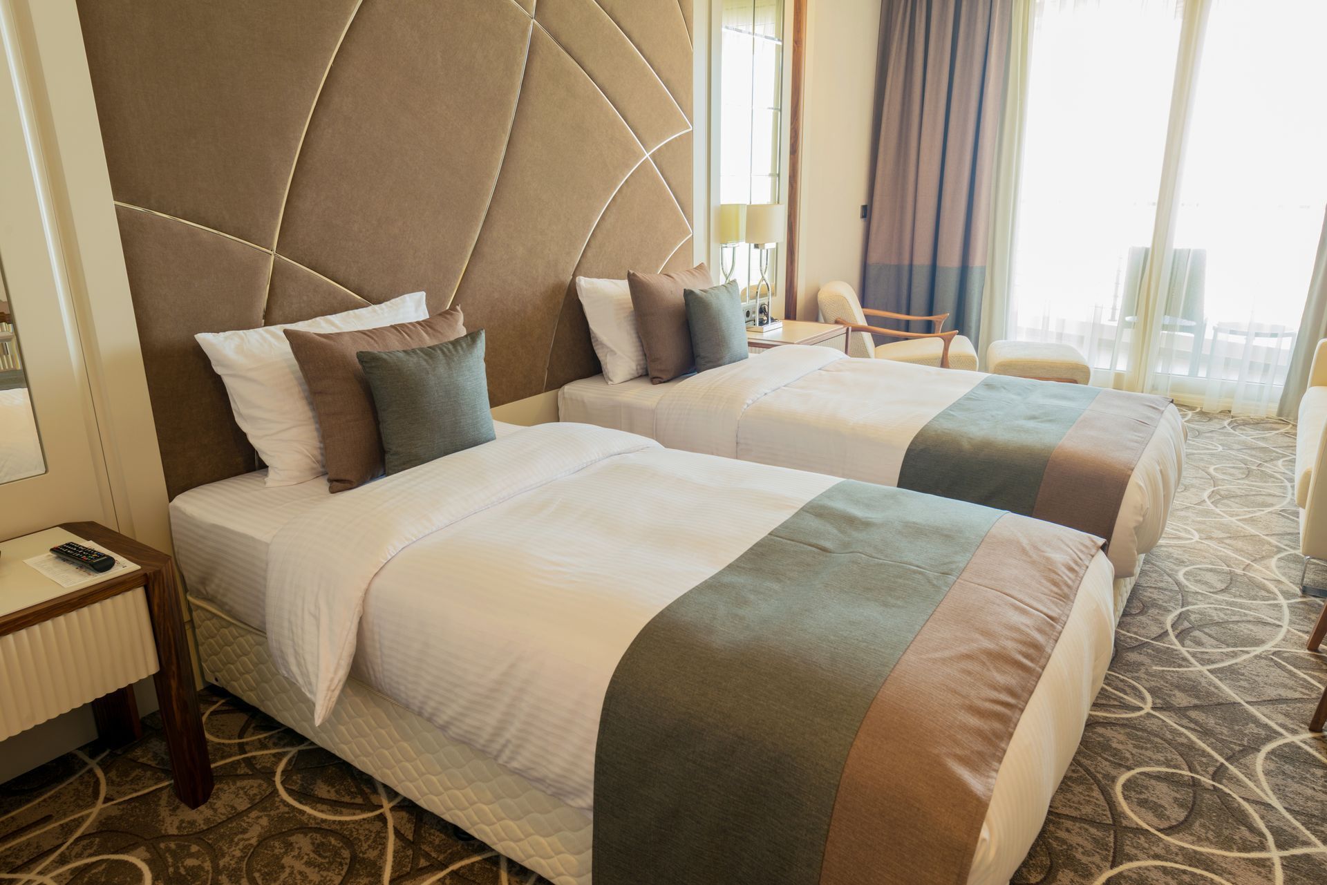 Zwei Einzelbetten in einem Hotelzimmer, beiges Kopfteil, graue und braune Akzente.