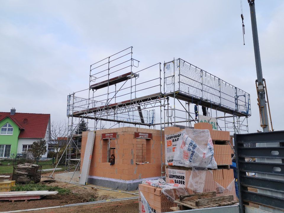 Haus im Bau mit Gerüst, Ziegeln und einem Kran, bewölkter Tag.