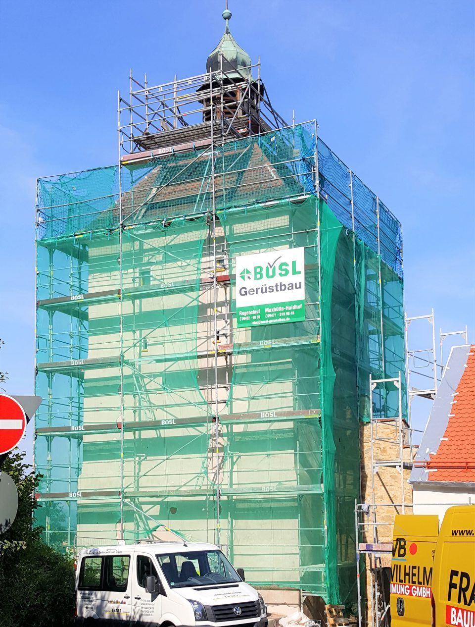 Gebäude im Umbau, mit grünem Netz und Gerüst bedeckt, davor parkt ein Lieferwagen.