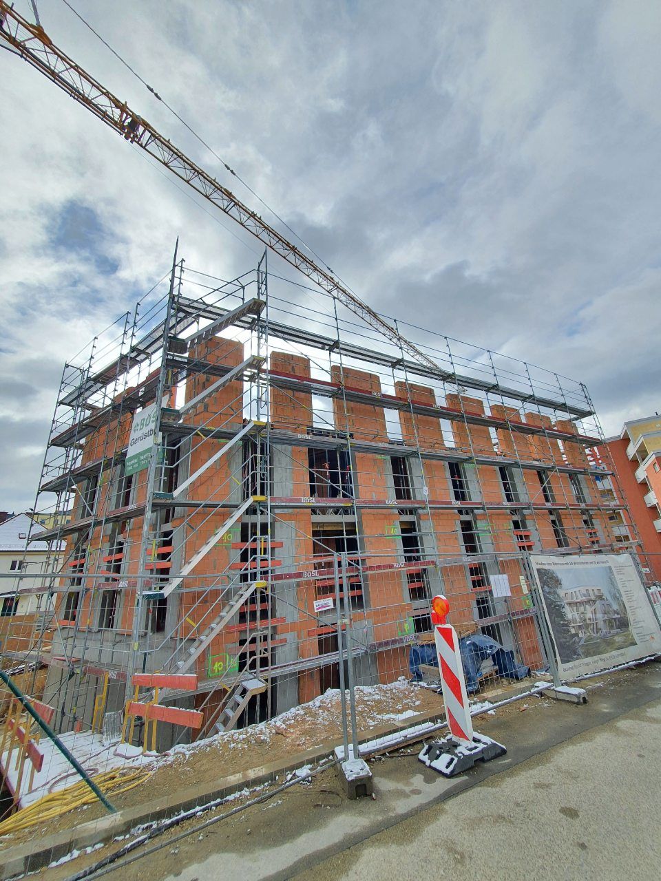 Baustelle: Mehrstöckiges Gebäude im Bau mit Gerüst und Kran, bewölkter Himmel.