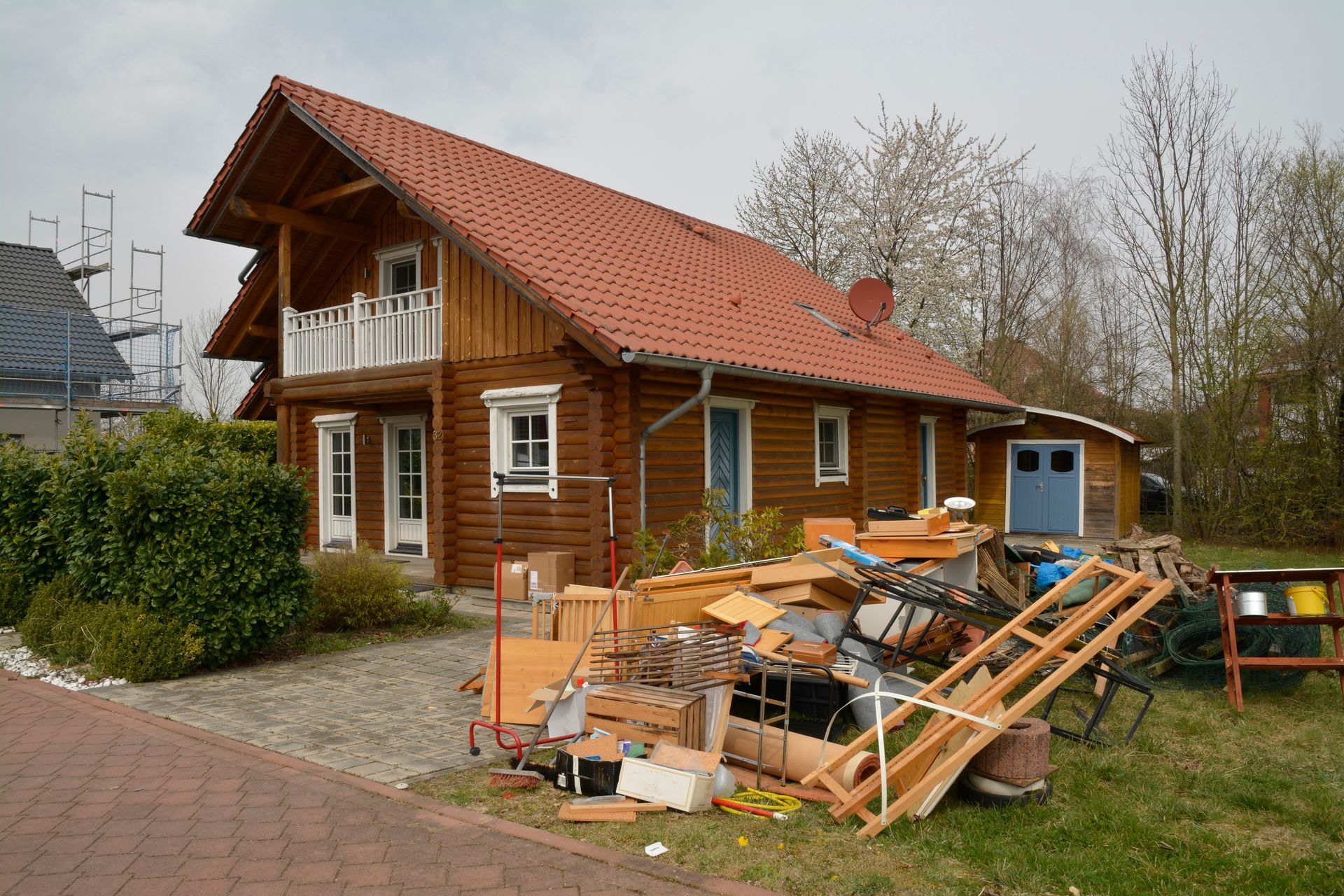 Braune Blockhütte mit rotem Dach; Rümpel von Entrümpelung im Vorgarten.