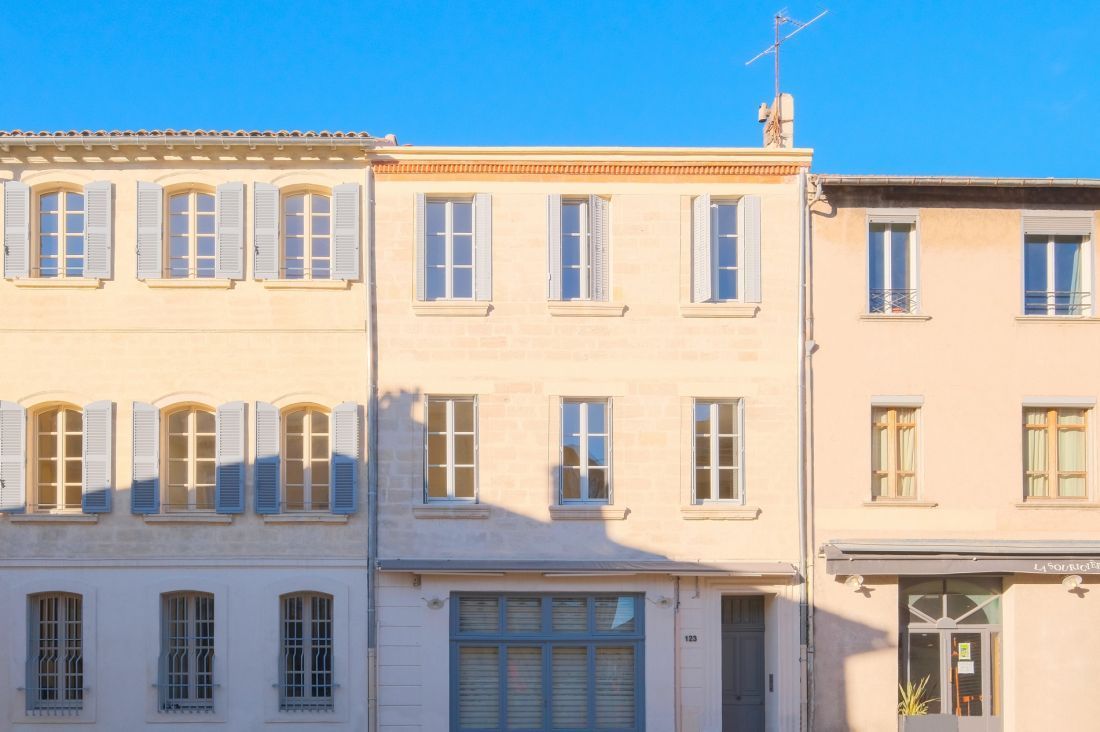 Rangée de bâtiments aux couleurs pastel avec des fenêtres et des volets bleus, se détachant sur un ciel bleu clair.