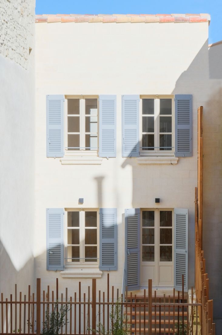 Bâtiment de deux étages couleur crème avec volets bleu clair aux fenêtres. 