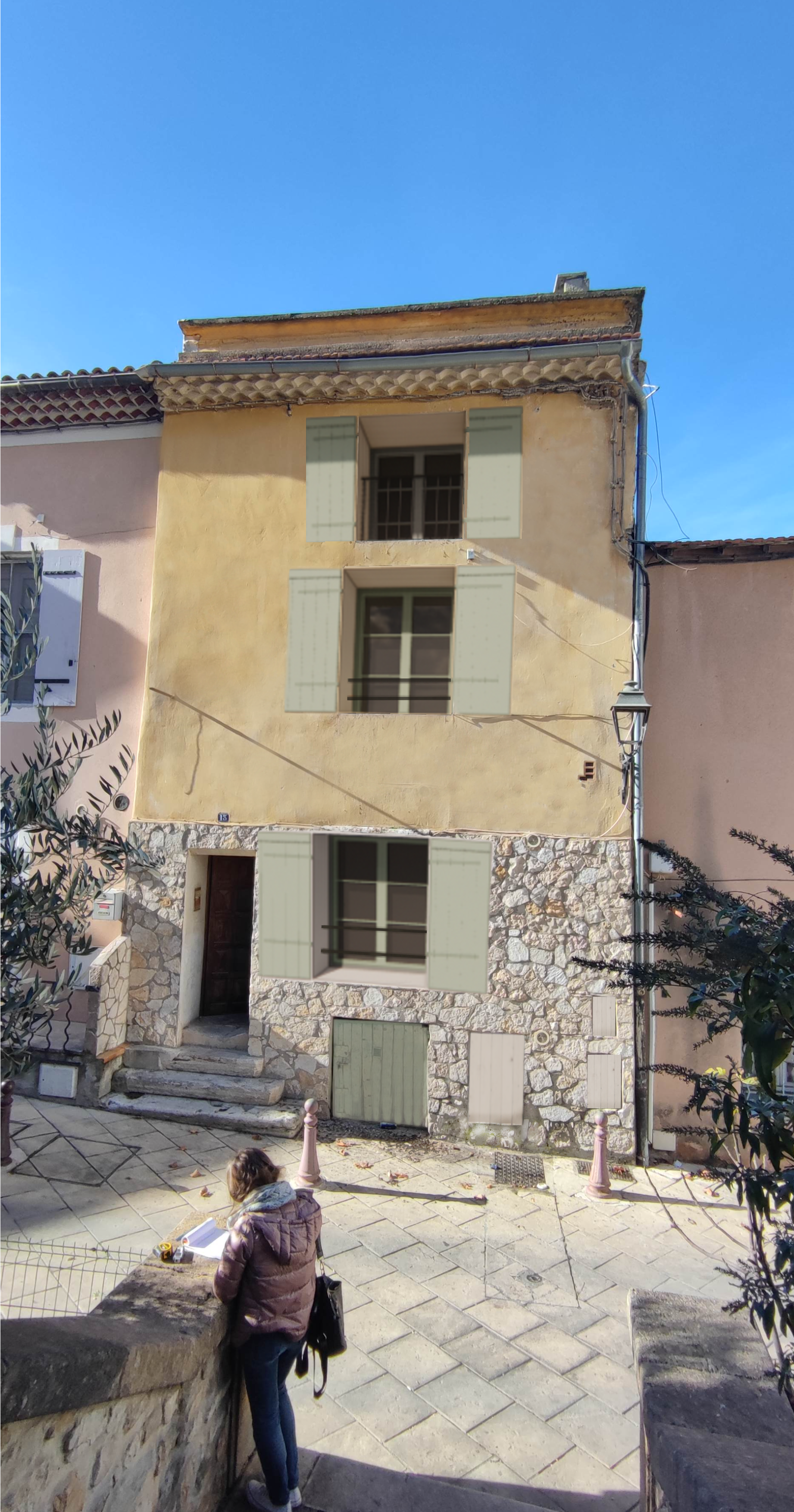Un bâtiment de trois étages avec une façade en pierre et en stuc jaune ; une personne dessine sur un mur au premier plan.