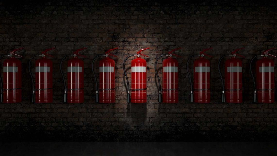 Fila de ocho extintores rojos montados en una pared de ladrillo oscuro.