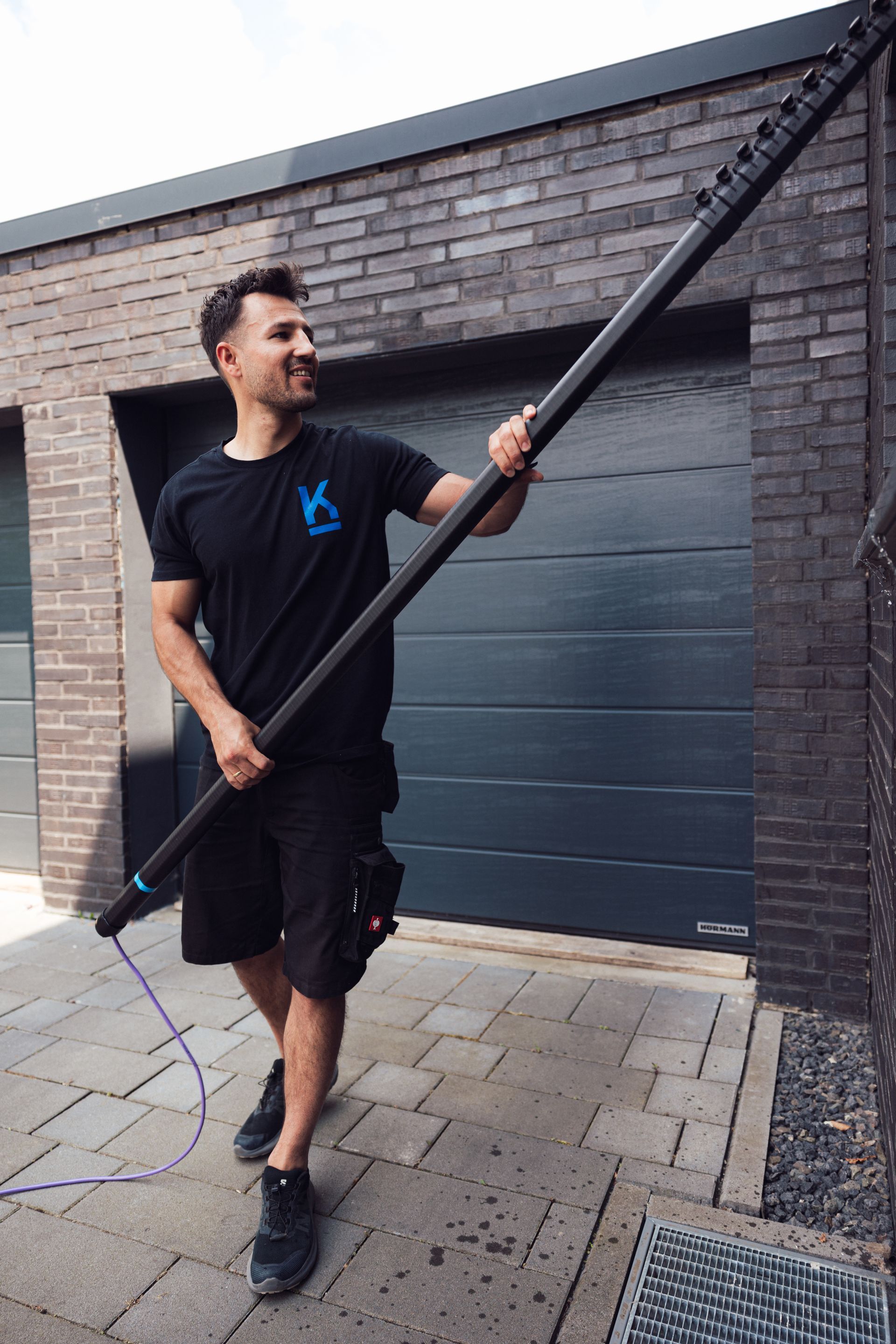 Ein Mann hält eine lange, schwarze Stange neben einem Backsteingebäude und reinigt die Oberfläche.