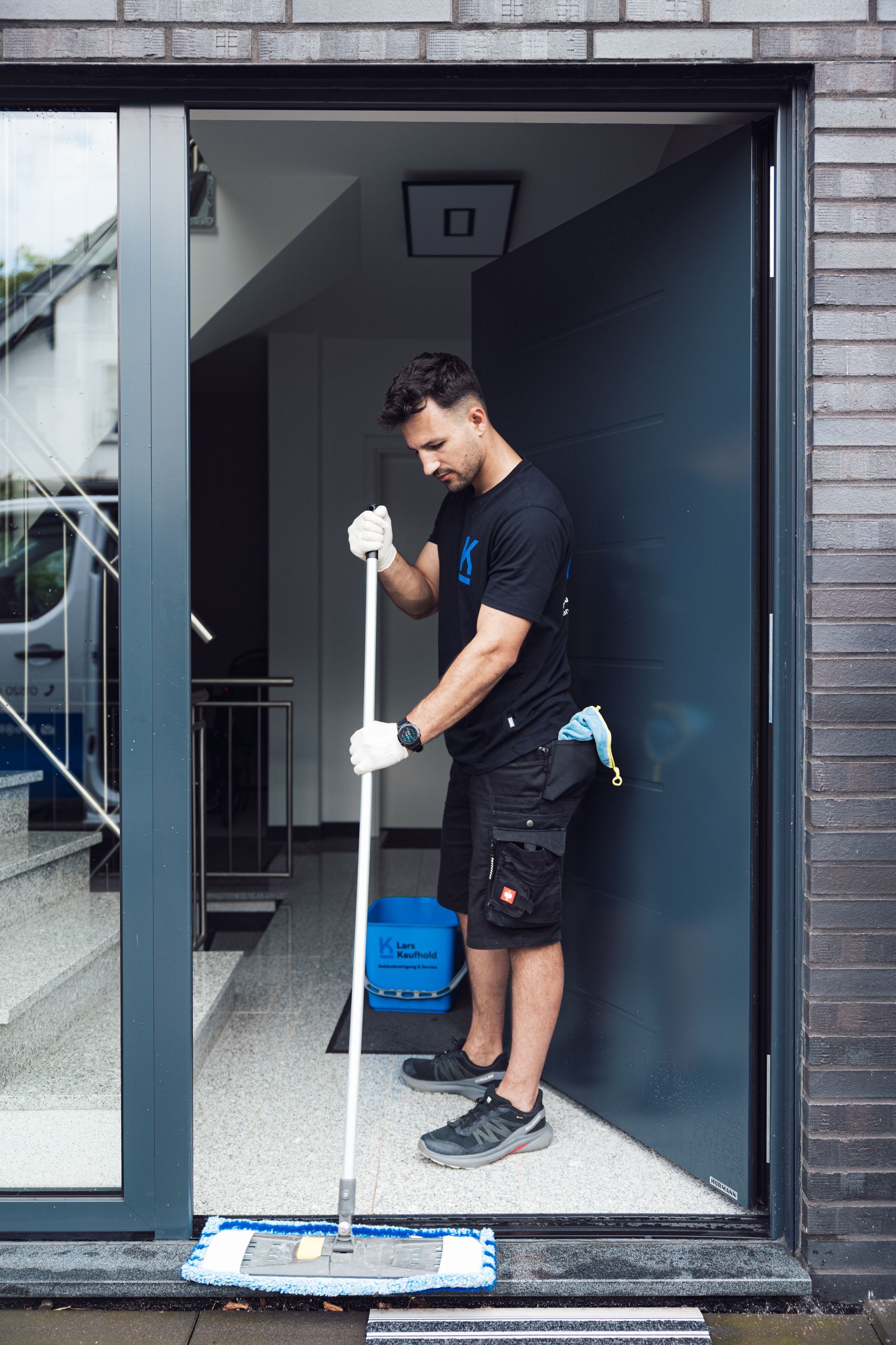 Ein Mann in Schwarz wischt mit einem Mopp einen Türrahmen.