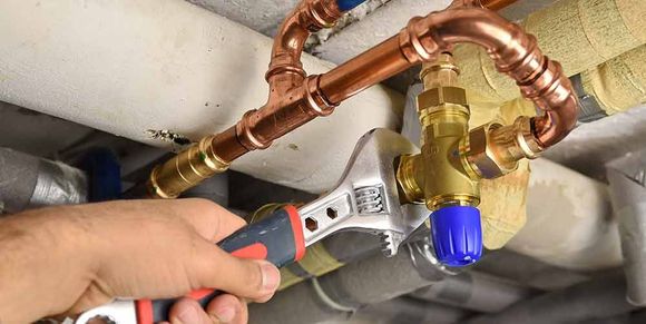 Eine Person arbeitet mit einem Schraubenschlüssel an einem Rohr.