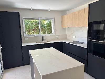 Cuisine moderne avec des meubles noirs, un îlot blanc et une fenêtre au-dessus de l’évier.