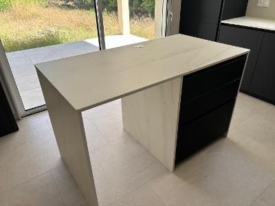 Bureau blanc avec des tiroirs noirs dans une pièce lumineuse près d’une porte vitrée.