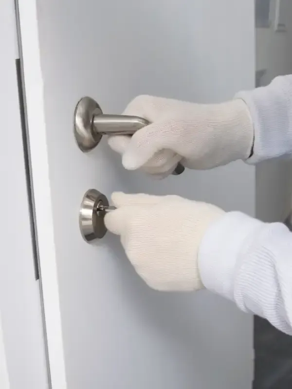 Persona con guantes blancos, abriendo una puerta con tirador y cerradura.