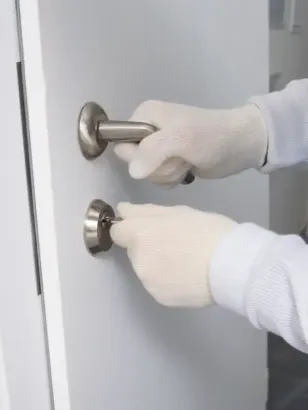 Persona con guantes blancos, abriendo una puerta con tirador y cerradura.