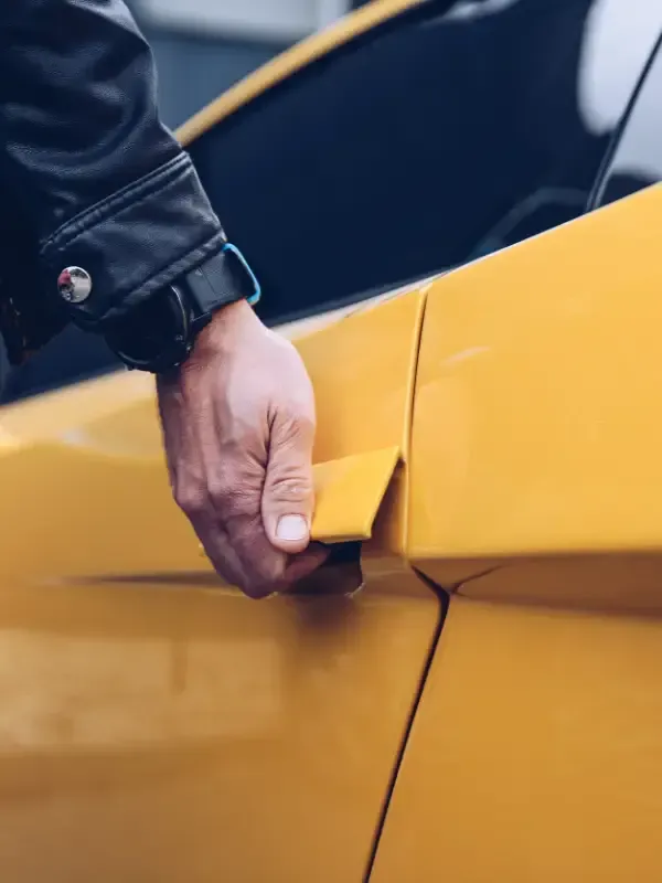 Mano de una persona con chaqueta de cuero negra abriendo la puerta de un coche amarillo.