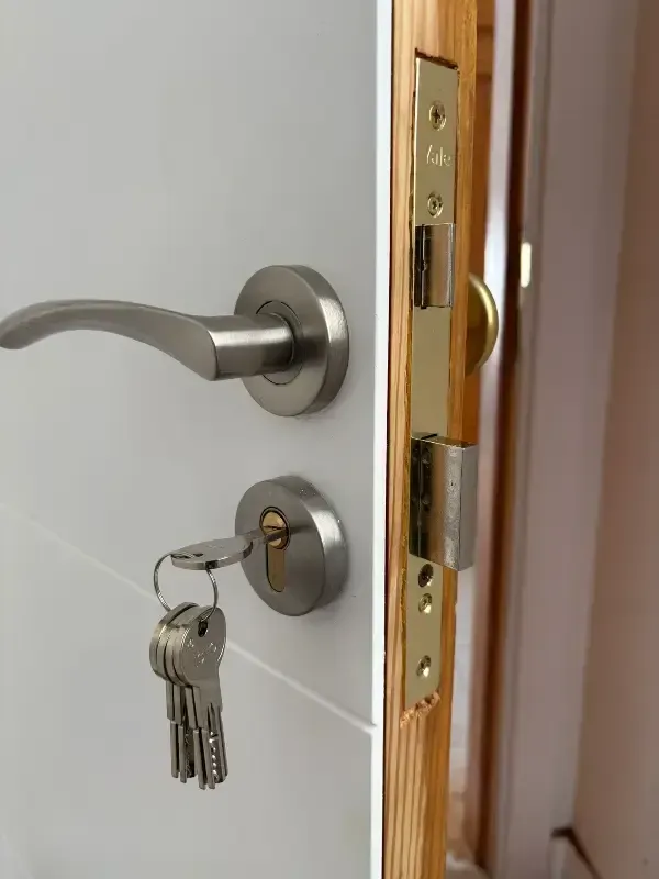 Puerta con manija y cerradura de níquel cepillado, con llaves en la cerradura. Pestillo dorado en el marco.