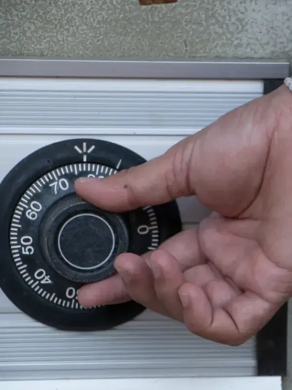 Mano girando el dial de combinación de una caja fuerte. El dial es negro con números blancos.