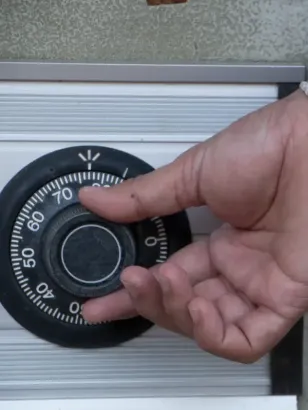 Mano girando el dial de combinación de una caja fuerte. El dial es negro con números blancos.