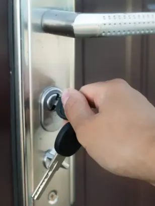 Mano insertando una llave en la cerradura de una puerta con manija plateada; abriendo la puerta.