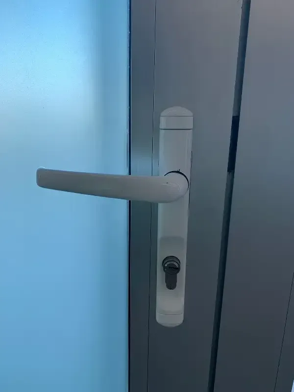 Manija de puerta blanca y ojo de cerradura en una puerta de vidrio azul claro.