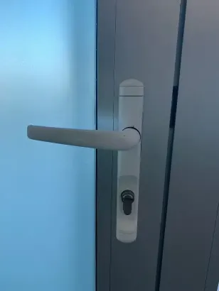 Manija de puerta blanca y ojo de cerradura en una puerta de vidrio azul claro.