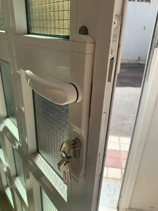 Puerta blanca con tirador y llave en la cerradura, vista parcial del exterior a través de una pequeña ventana.