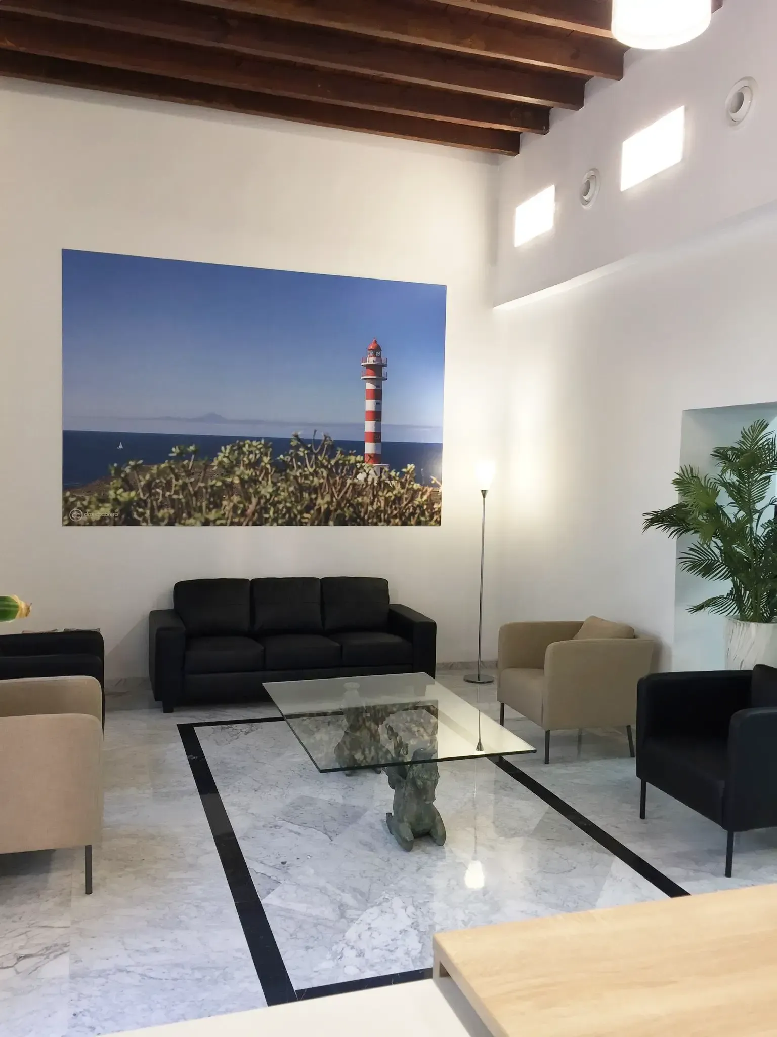 Área de recepción con piso de mármol blanco, pared verde claro, sofás negros y tostados y grandes ventanales.