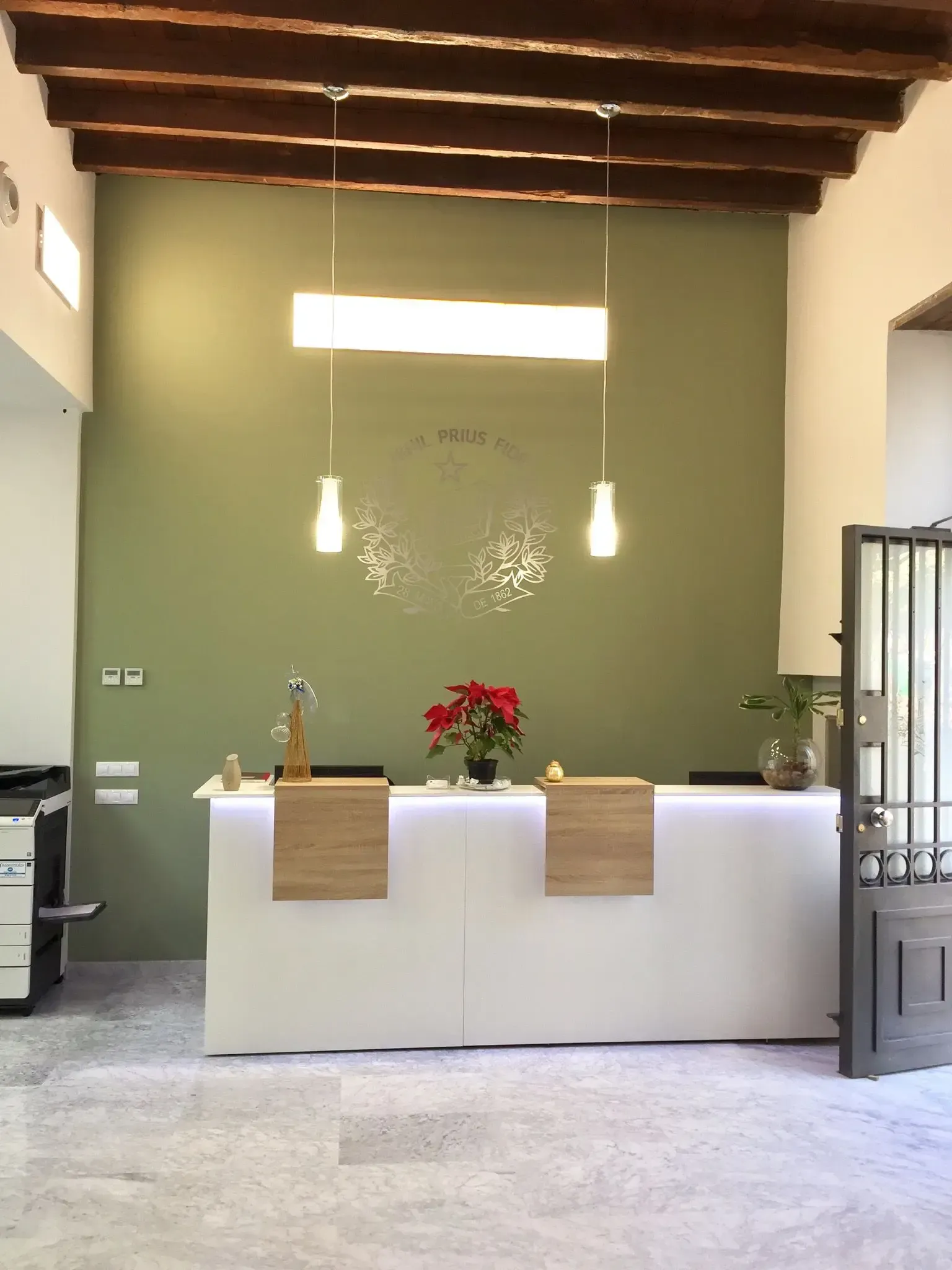 Área de recepción con piso de mármol blanco, pared verde claro, sofás negros y tostados y grandes ventanales.