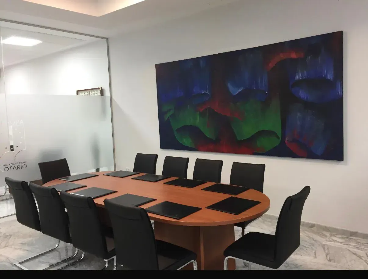 Una sala de conferencias con una mesa de cristal, sillas negras y un barco decorativo en la pared. Una maceta en la esquina.