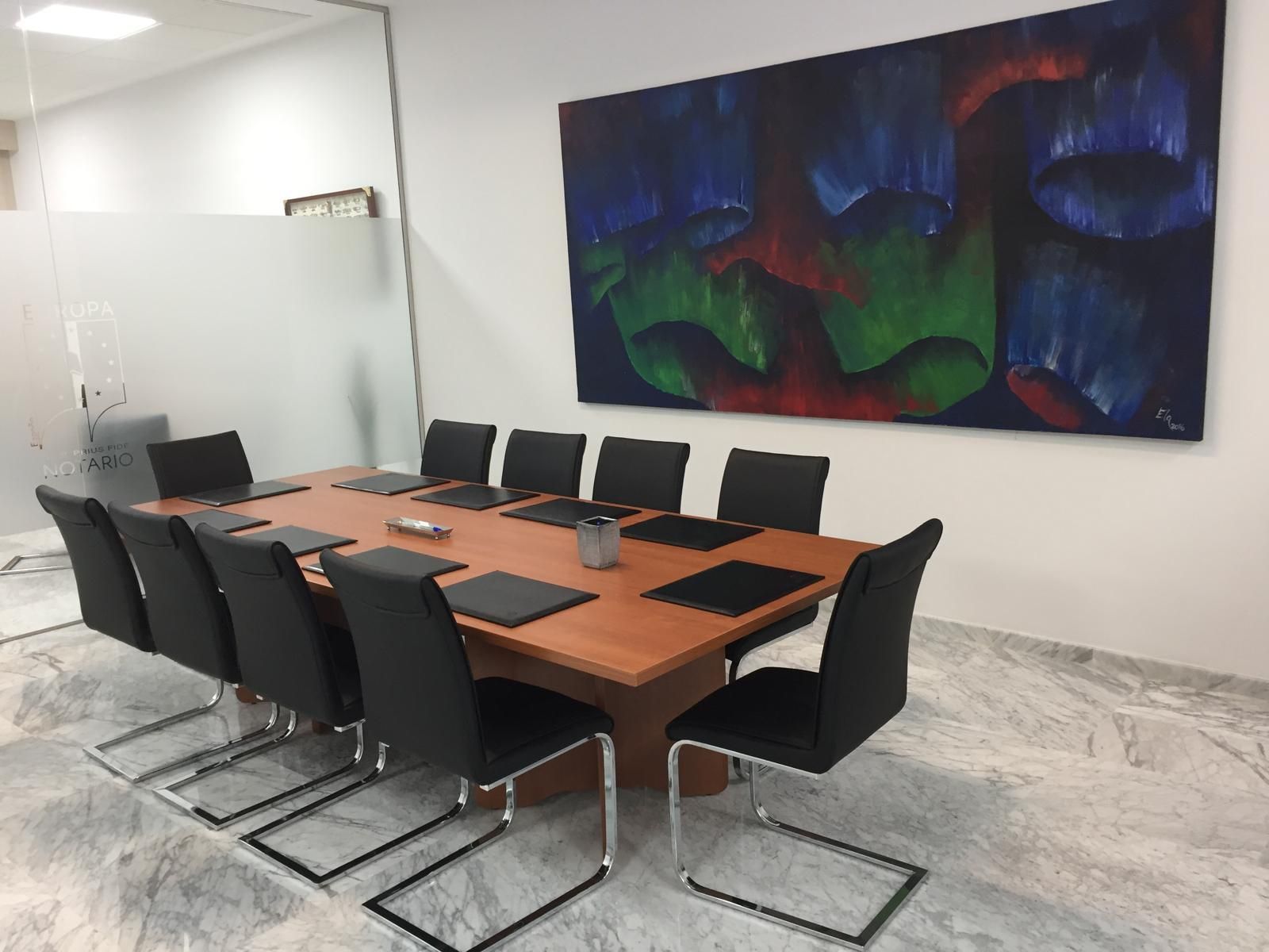 Una sala de conferencias con una mesa de cristal, sillas negras y un barco decorativo en la pared. Una maceta en la esquina.