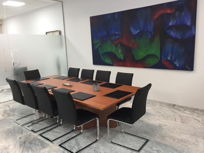 Una sala de conferencias con una mesa de cristal, sillas negras y un barco decorativo en la pared. Una maceta en la esquina.