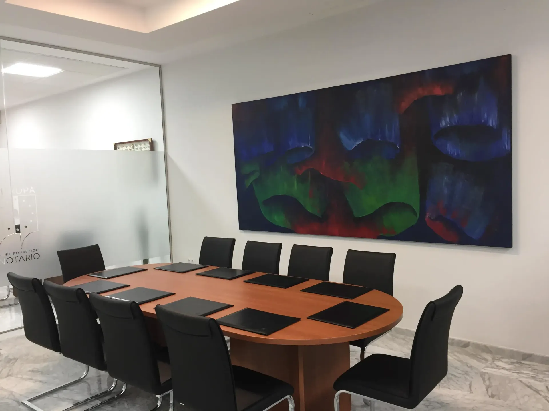 Una sala de conferencias con una mesa de cristal, sillas negras y un barco decorativo en la pared. Una maceta en la esquina.