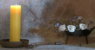 Una vela amarilla está sobre una mesa al lado de un jarrón con flores.