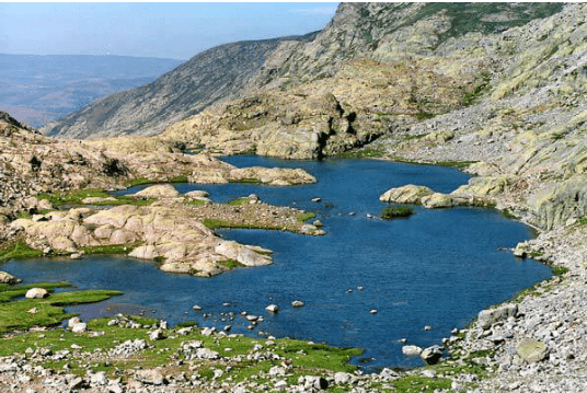 Un lago en medio de una montaña rodeado de rocas y hierba.