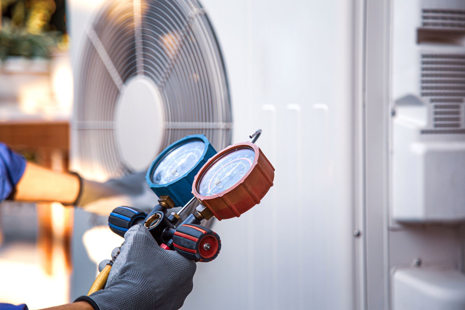 Main gantée tenant des manomètres de climatisation à côté d’un climatiseur extérieur