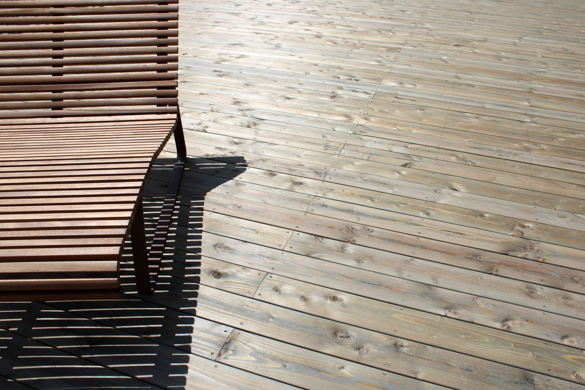 Un banc en bois projette des ombres sur une passerelle en bois.