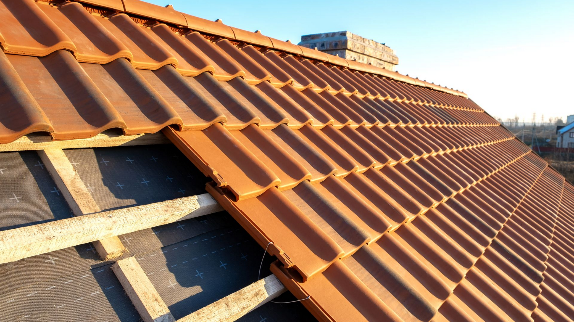 Pose de tuiles en terre cuite sur un toit aux poutres en bois apparentes.