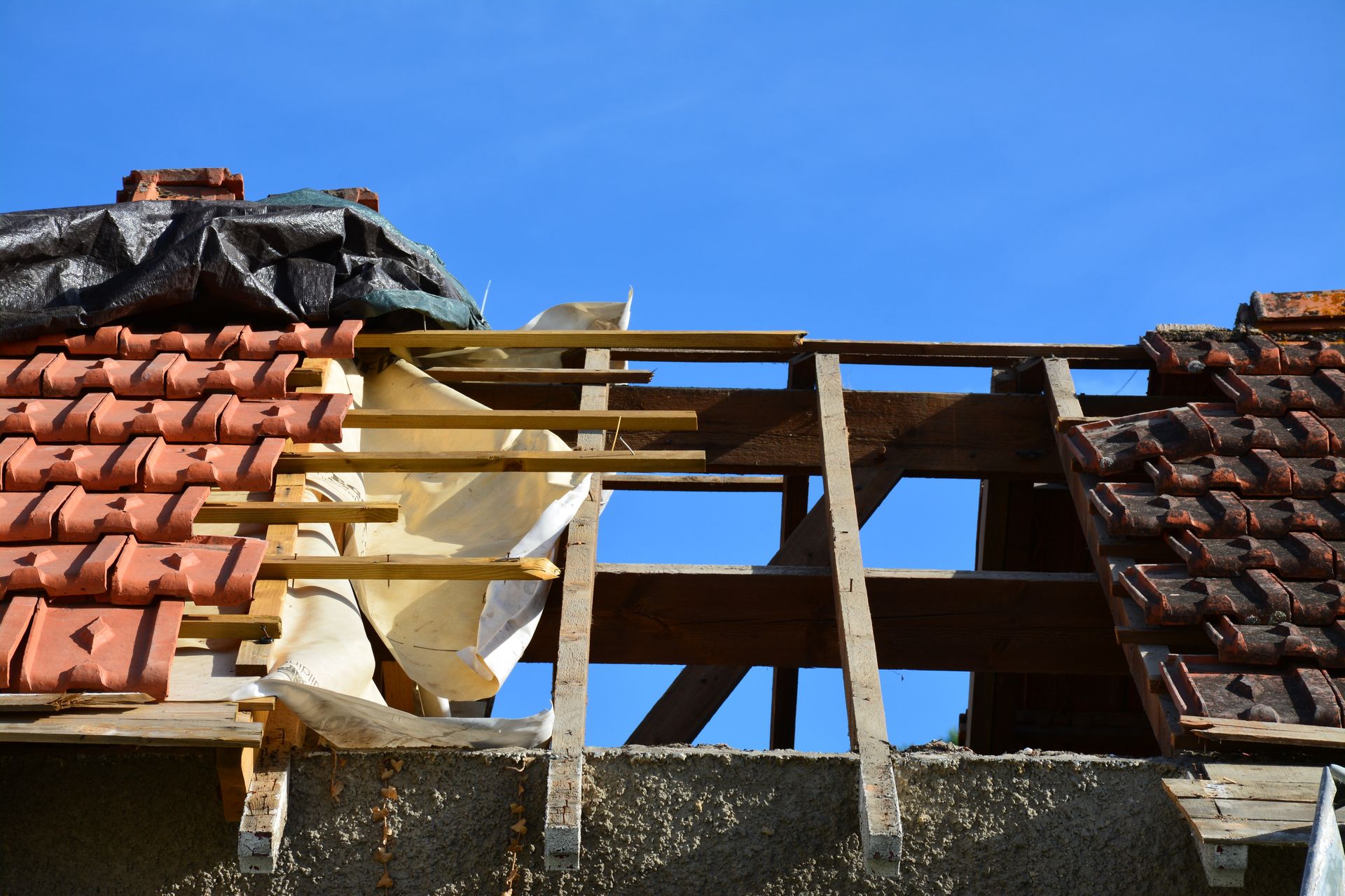 Toiture partiellement démontée, laissant apparaître des poutres en bois et des tuiles manquantes.