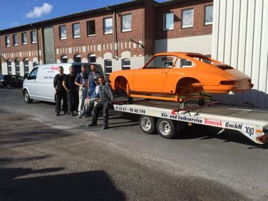 eam von Kfz & Lackservice Bieniek GmbH mit orangefarbenem Fahrzeug auf Ladefläche