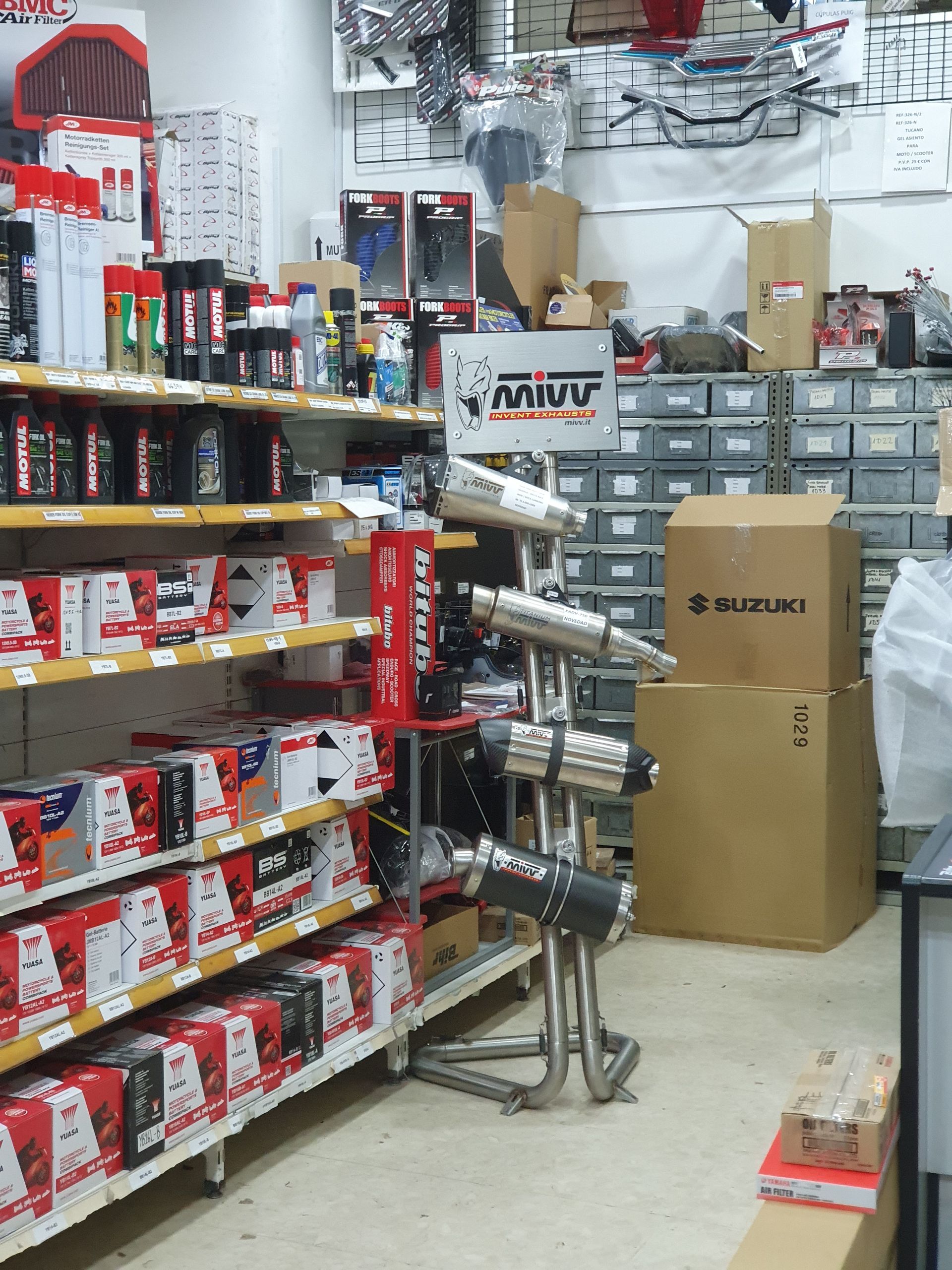 Tienda de repuestos para motocicletas con estantes llenos de productos y tubos de escape exhibidos en un soporte.