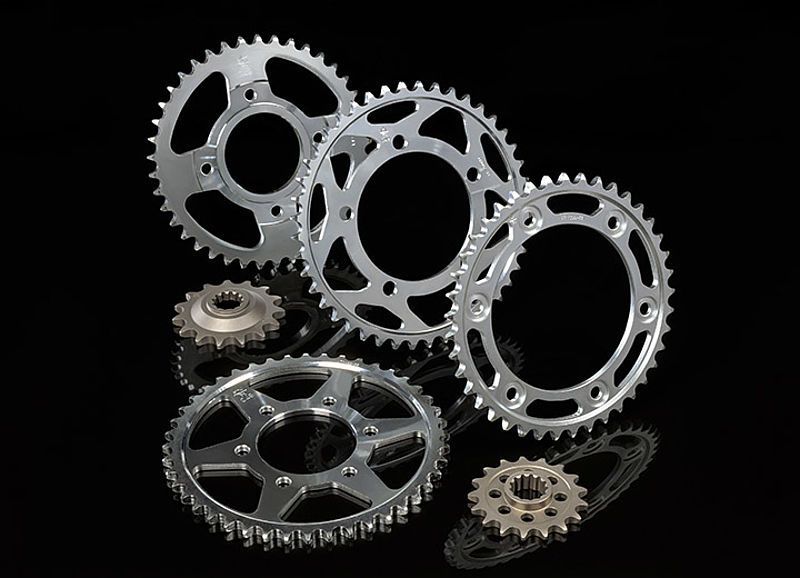 Piñones de motocicleta de metal brillante dispuestos sobre una superficie reflectante negra.