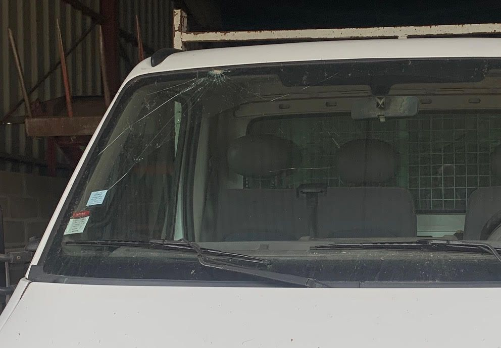 Vue de face d'une camionnette blanche stationnée à l'intérieur, montrant le pare-brise et les sièges avant à travers la vitre.