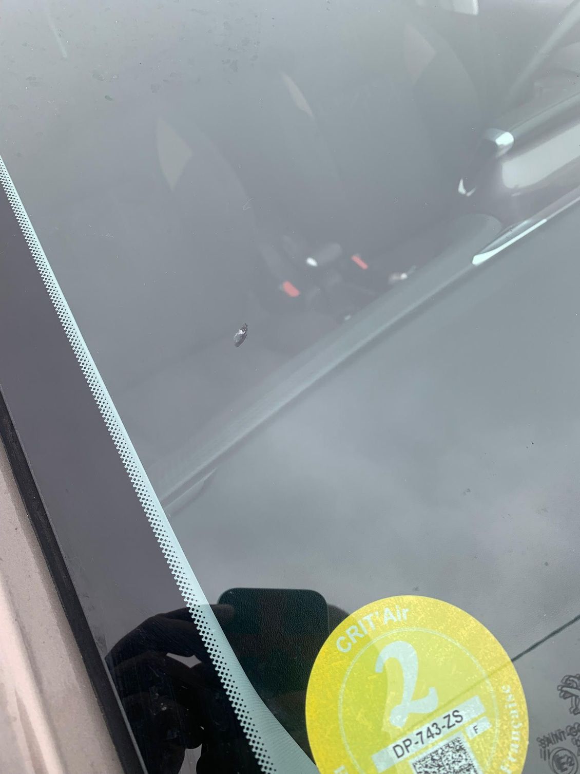 Pare-brise de voiture avec une vignette de contrôle technique jaune et des reflets du tableau de bord dans le coin
