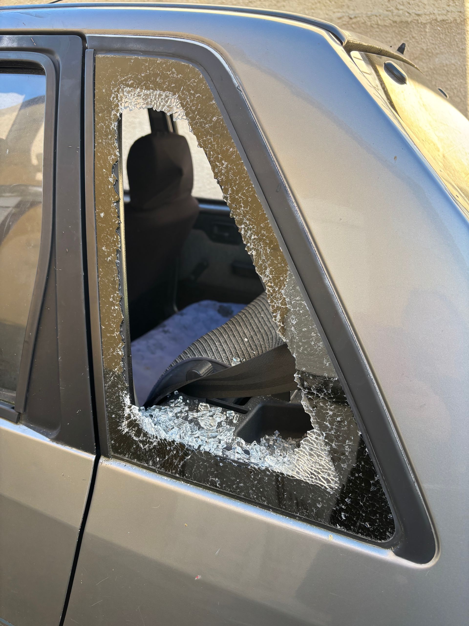 Vitre de voiture brisée, verre en éclats et cadre tordu sur une portière de véhicule beige