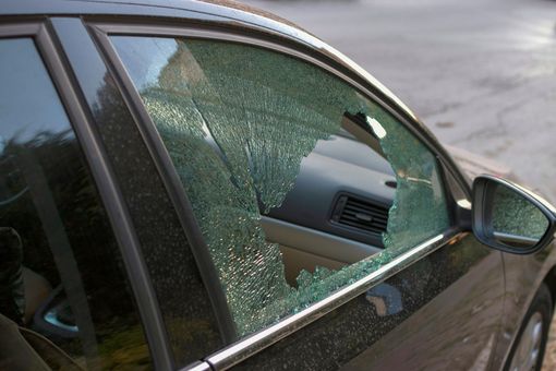 Vitre latérale brisée d'une voiture noire, vue de l'extérieur.