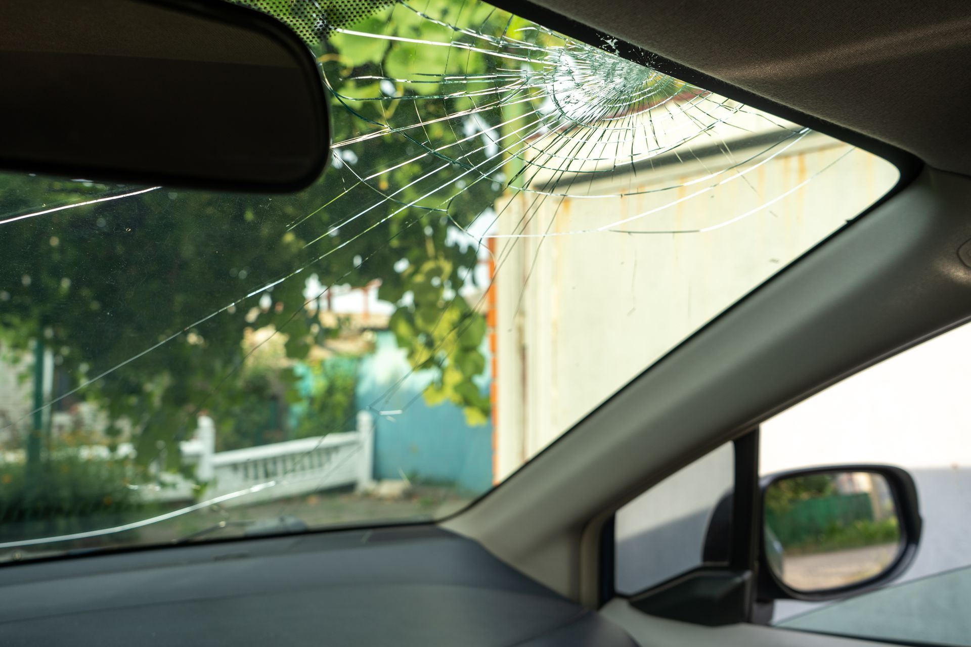 Intérieur de la voiture donnant sur une allée pluvieuse, une clôture blanche et des arbres à l'extérieur, par la fenêtre latérale