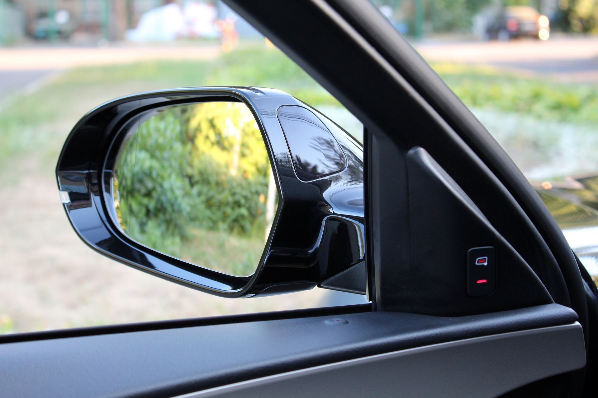 Le rétroviseur latéral de la voiture reflète un bord de route vert flou, vu de l'intérieur du véhicule.